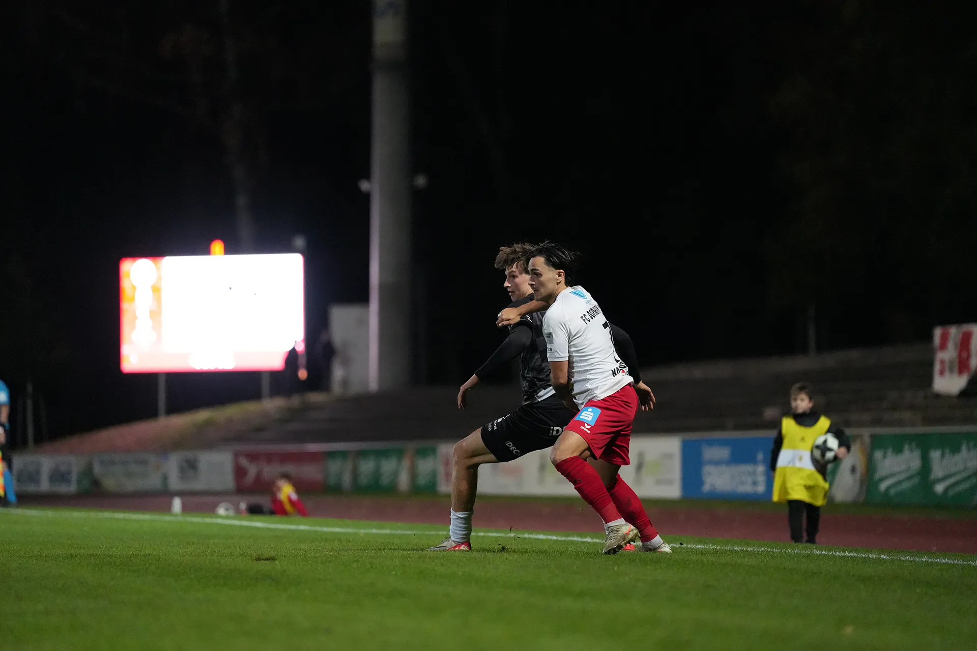 Fußballspieler in Aktion auf dem Spielfeld, im Hintergrund eine Anzeigetafel